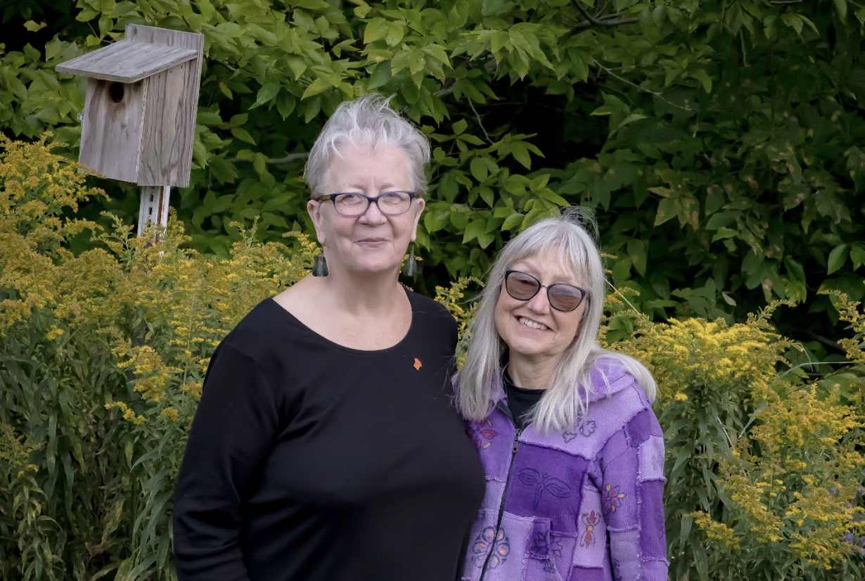 Winifred and Leslie standing side by side with foliage and a bird feeder in the background. Courage & Renewal ® Courage Retreats, Circle of Trust ®, Courage to Teach ® image.